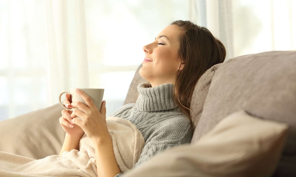 A woman sitting on the couch relaxing from the heat with an air conditioner